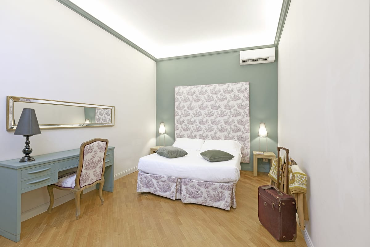 A bedroom with a bed, a desk, a chair, a lamp, and a suitcase.