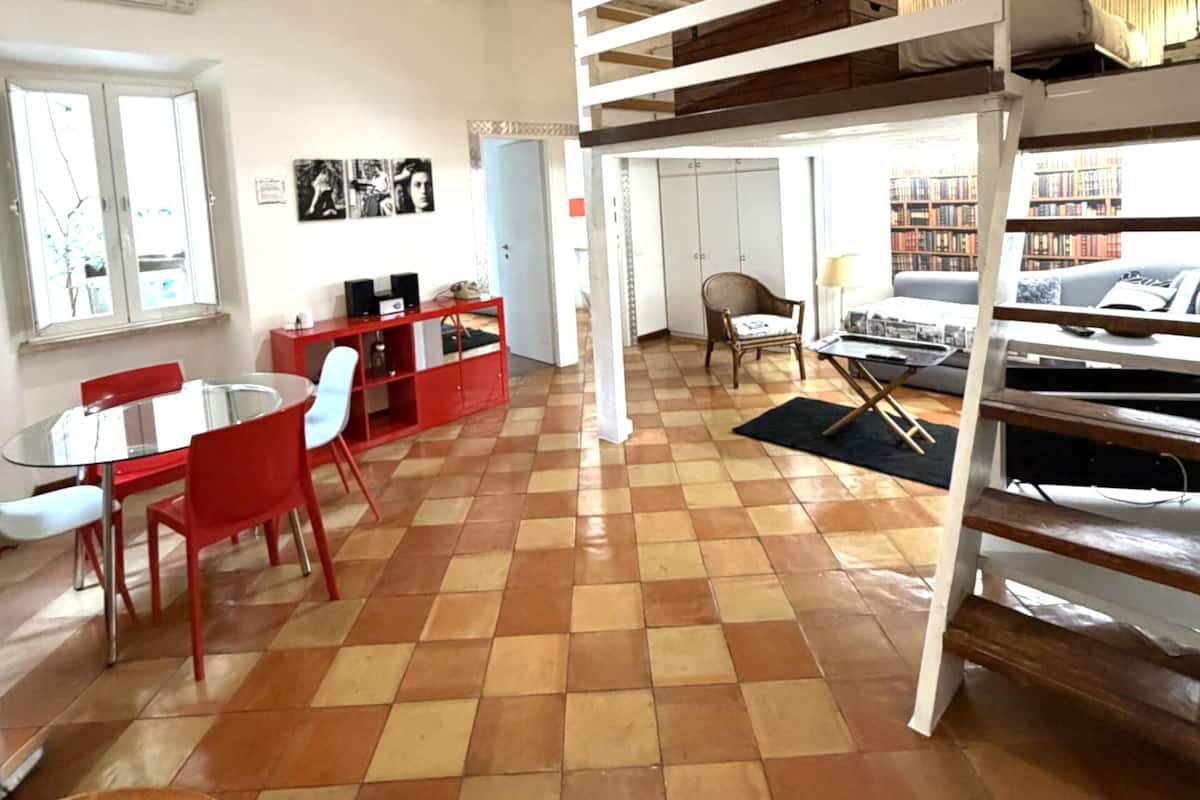 A room with a checkered floor, a bunk bed, a dining table with chairs, a red cabinet, and a bookshelf.