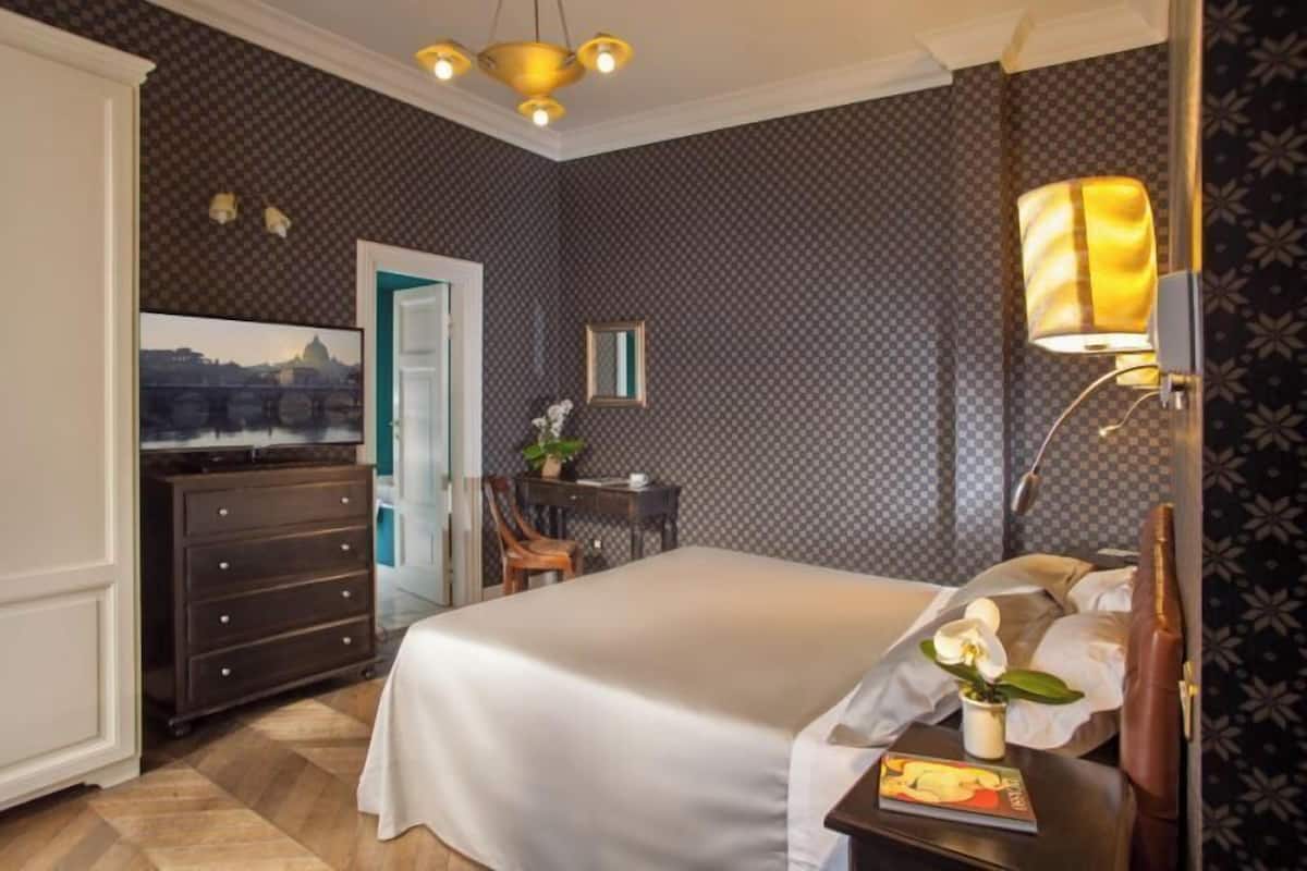 A hotel room with a bed, a desk, a chair, a dresser, a television, and a lamp.
