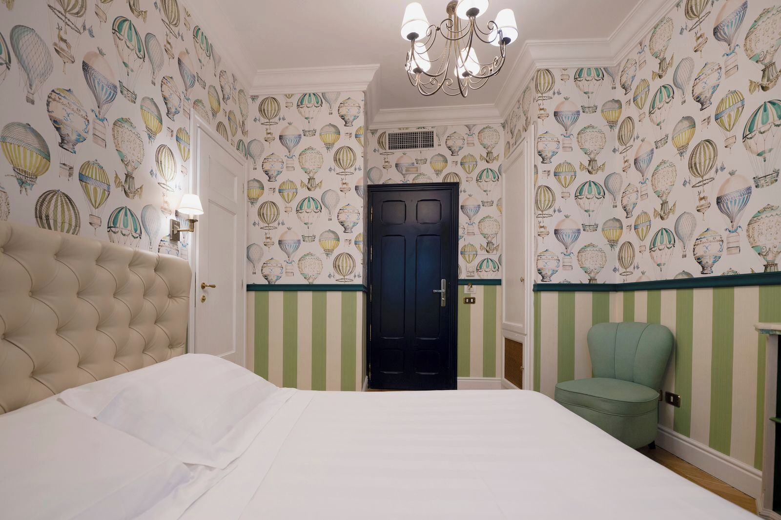 A bedroom with a large bed, a green chair, a black door, and wallpaper with hot air balloon designs.