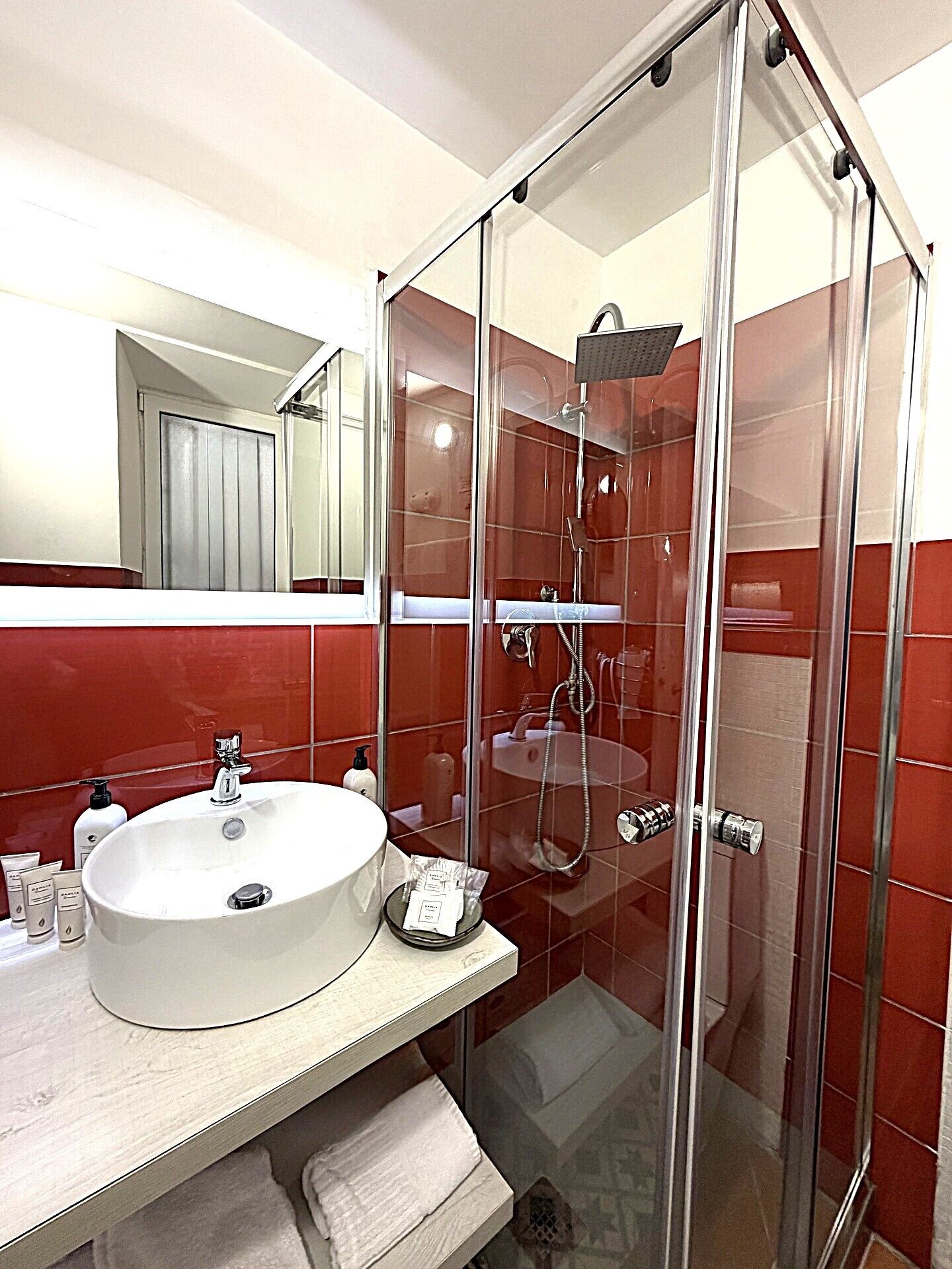 Un baño con cabina de ducha de vidrio, un lavamanos blanco y paredes con baldosas rojas.
