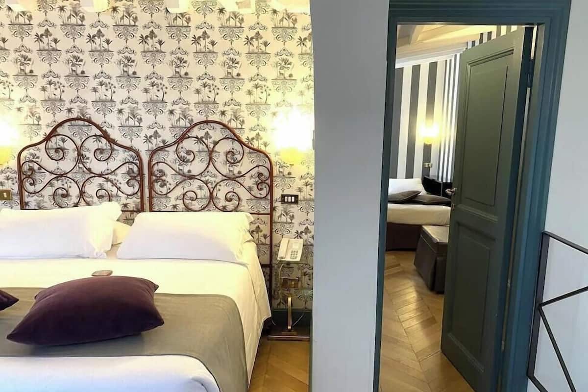 A double bed with a decorative headboard, a bedside telephone, and a patterned wallpaper.