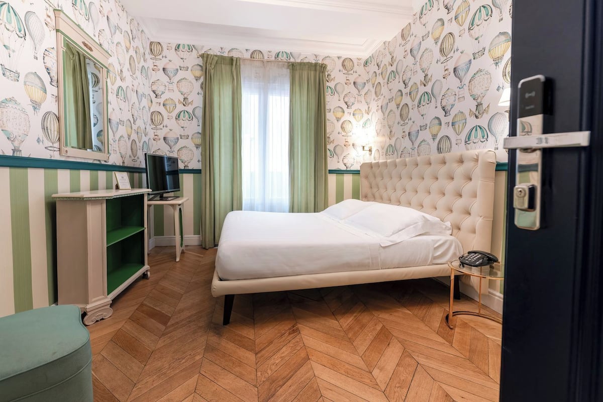 A hotel room with a bed, a desk, a television, and a door with a lock.