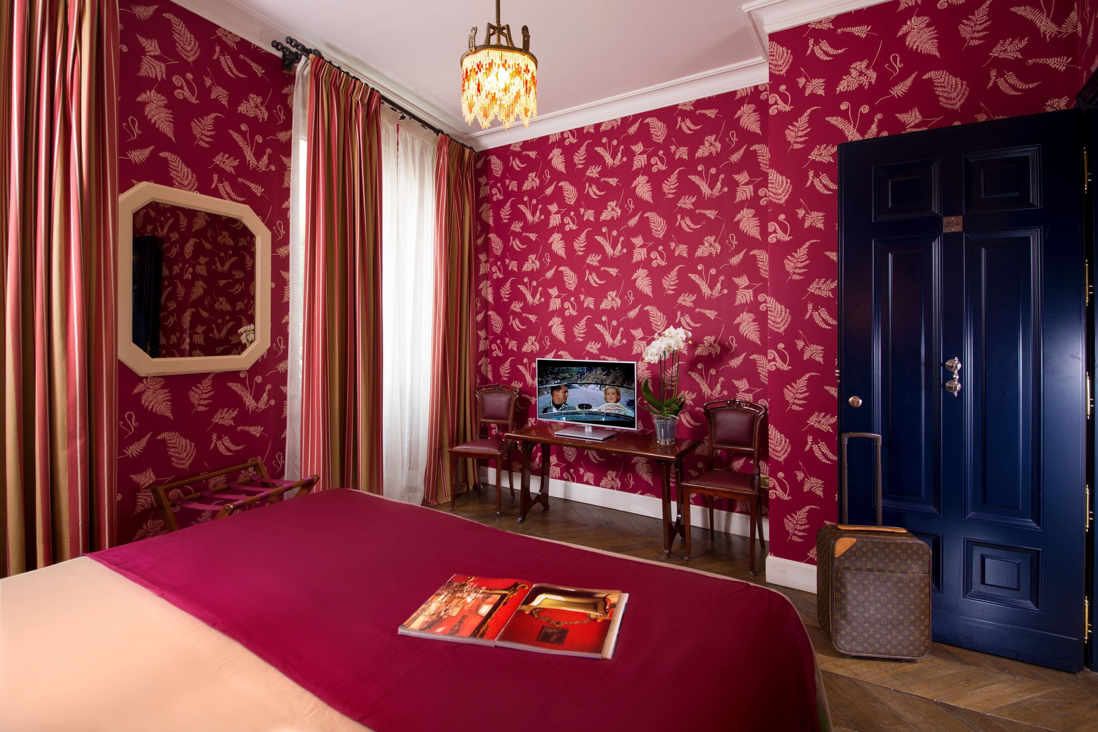 A hotel room with a large bed, a desk with a laptop, a television, and a blue door.