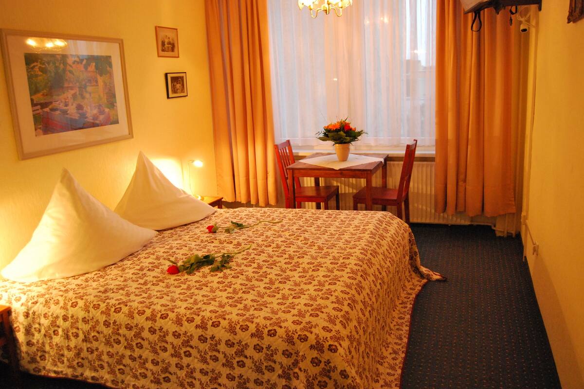 A hotel room with a bed, a table with chairs, and a window with curtains.