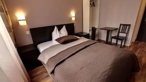 A hotel room with a large bed, two bedside tables, a chair, and a small desk. - Pension ABC (Berlin)