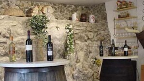 A rustic interior with a stone wall, wooden barrel, and wine bottles on a counter. - La Voce del Vento (Pastena)