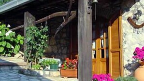 A rustic stone building with a wooden porch, potted plants, and a wooden door. - La Voce del Vento (Pastena)