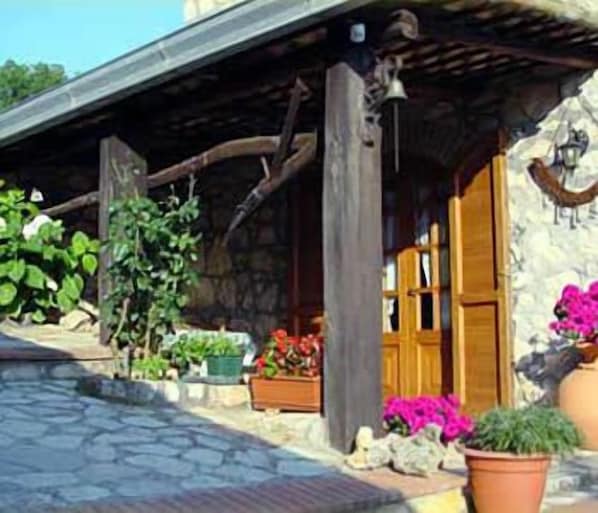 A rustic stone building with a wooden porch, potted plants, and a wooden door.
