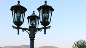A street lamp with three lights, surrounded by greenery and a view of distant hills. - La Voce del Vento (Pastena)