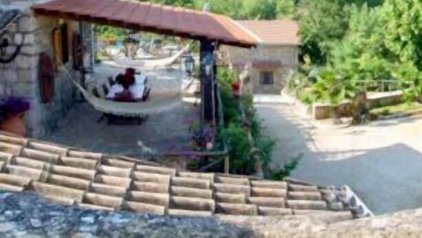 A stone building with a covered outdoor seating area, a staircase leading to a higher level, and a lush green hillside in the background. - La Voce del Vento (Pastena)
