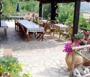 An outdoor patio with stone flooring, wooden tables and chairs, and potted plants.