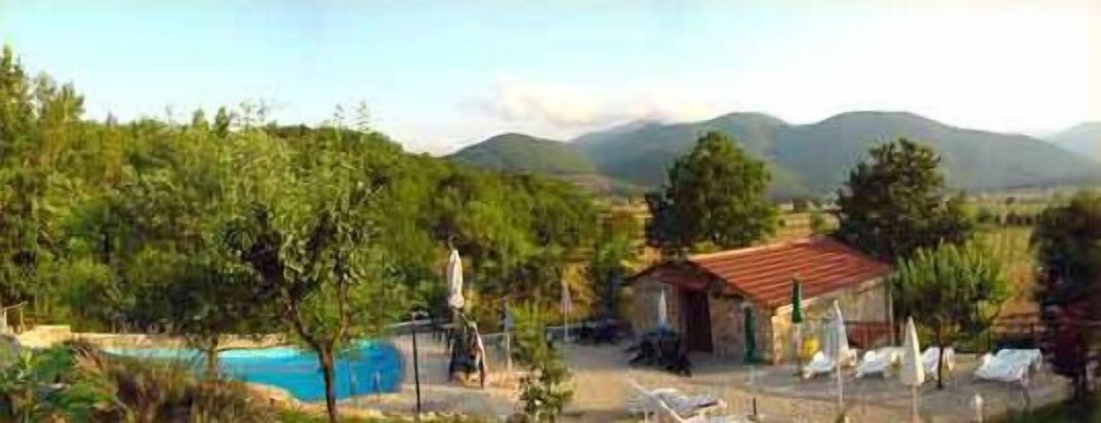 Un área de piscina con sillas de descanso, un edificio pequeño y montañas al fondo.