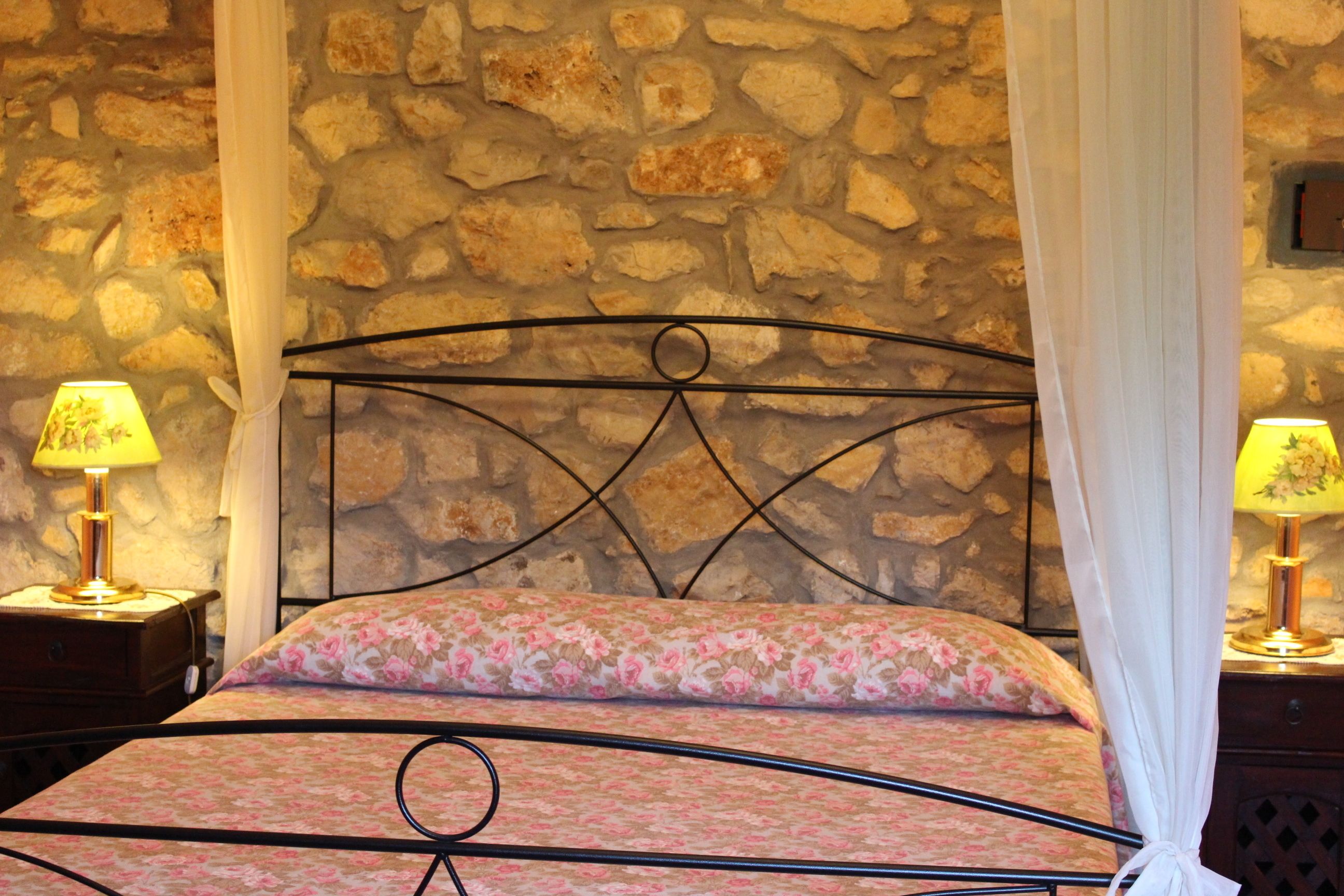 A bed with a metal frame and a floral bedspread, set against a stone wall.