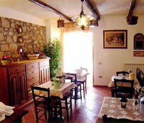 A dining area with a stone wall, wooden cabinets, and a table with chairs. There is a plant, a hanging light fixture, and a painting on the wall.