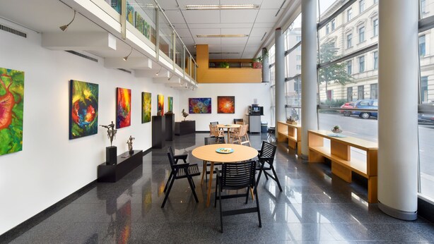 Una galería de arte moderno con una mesa redonda central y sillas, rodeada de pinturas coloridas en las paredes.