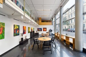 Una galleria d'arte moderna con un tavolo rotondo al centro e sedie, circondata da dipinti colorati alle pareti.
