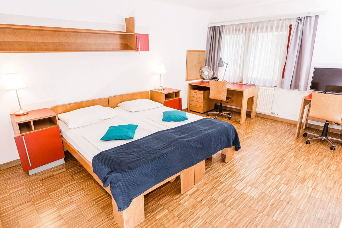 Una camera d'albergo con un letto, una scrivania, una sedia, una televisione e un armadio.