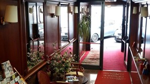 Un hall de hotel con alfombra roja, una mesa de recepción y un ventanal con vista a un coche estacionado afuera.