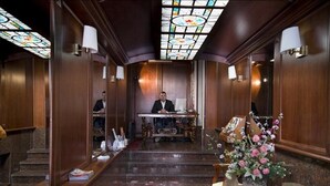 Un vestíbulo de hotel con una escalera monumental, una recepción y un techo de vitrales.