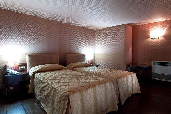 Una habitación con dos camas, un escritorio, una lámpara y un calefactor en la pared.