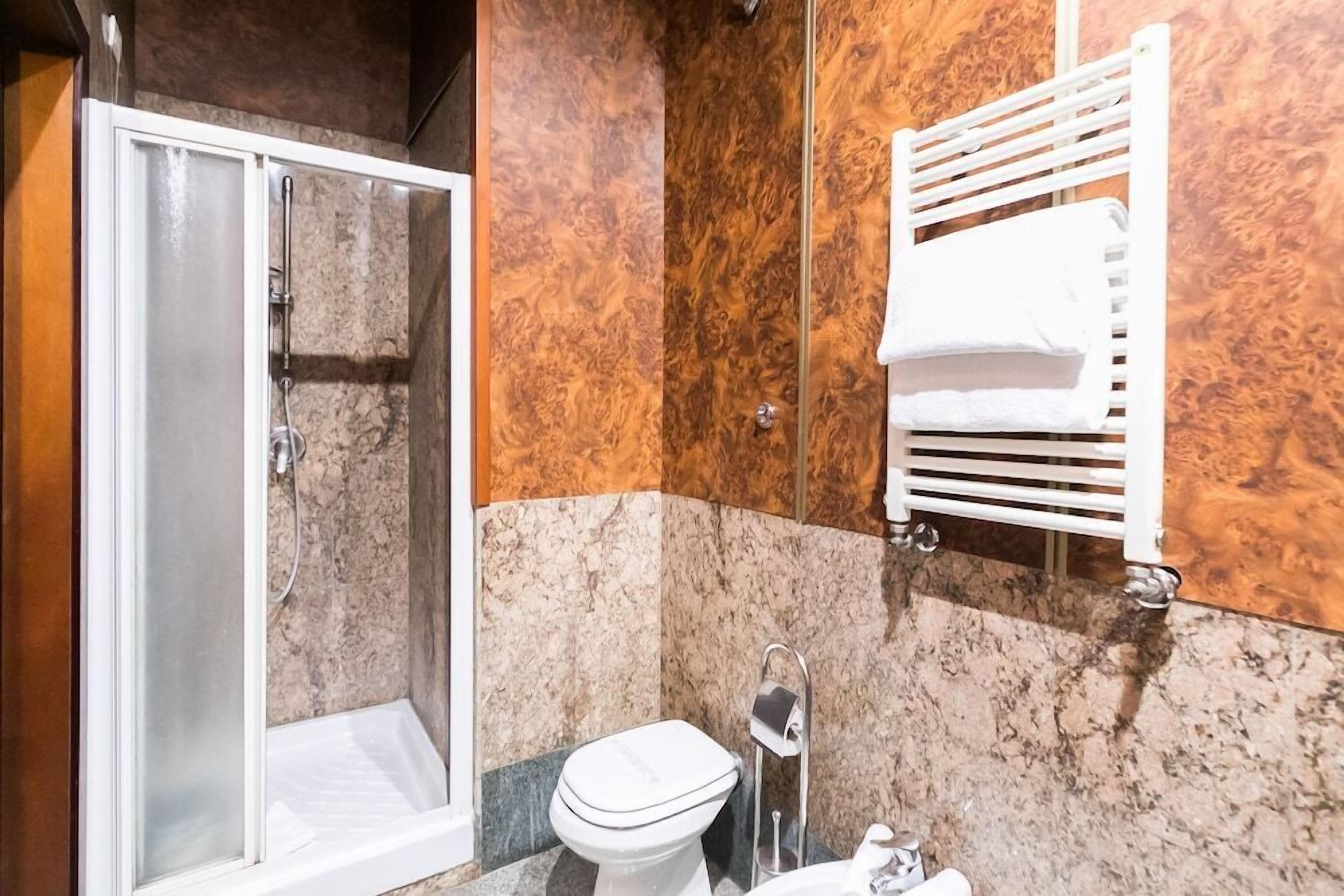 A bathroom with a glass-enclosed shower, a toilet, and a towel rack.