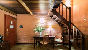 Una escalera de madera que conduce a un piso superior, una mesa de comedor con sillas, un jarrón con flores y una lámpara.