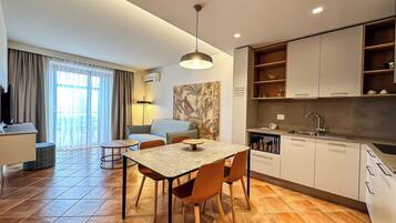 A modern hotel room with a dining area, kitchenette, and a large window with curtains.