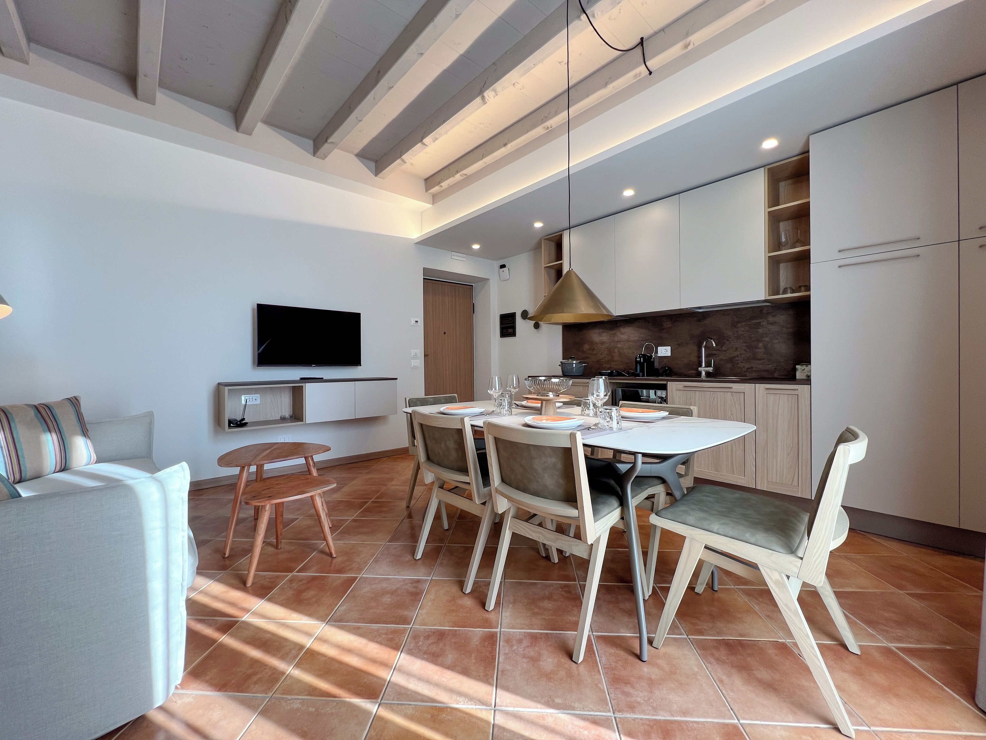 A modern living room with a dining area, a TV mounted on the wall, and a kitchen with wooden cabinets.