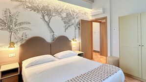 A bedroom with a large bed, wooden headboard, a nightstand, a wall-mounted lamp, and a wardrobe.