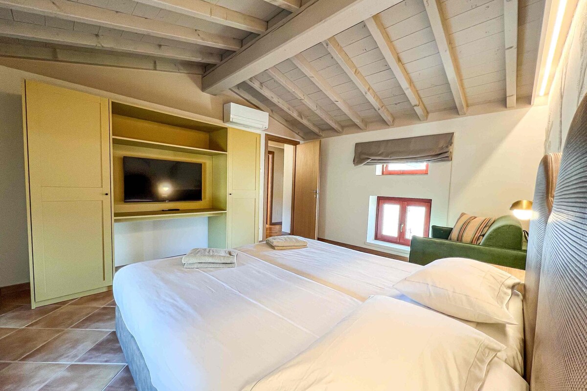 A bedroom with a large bed, a TV on a shelf, a window, and a green chair.
