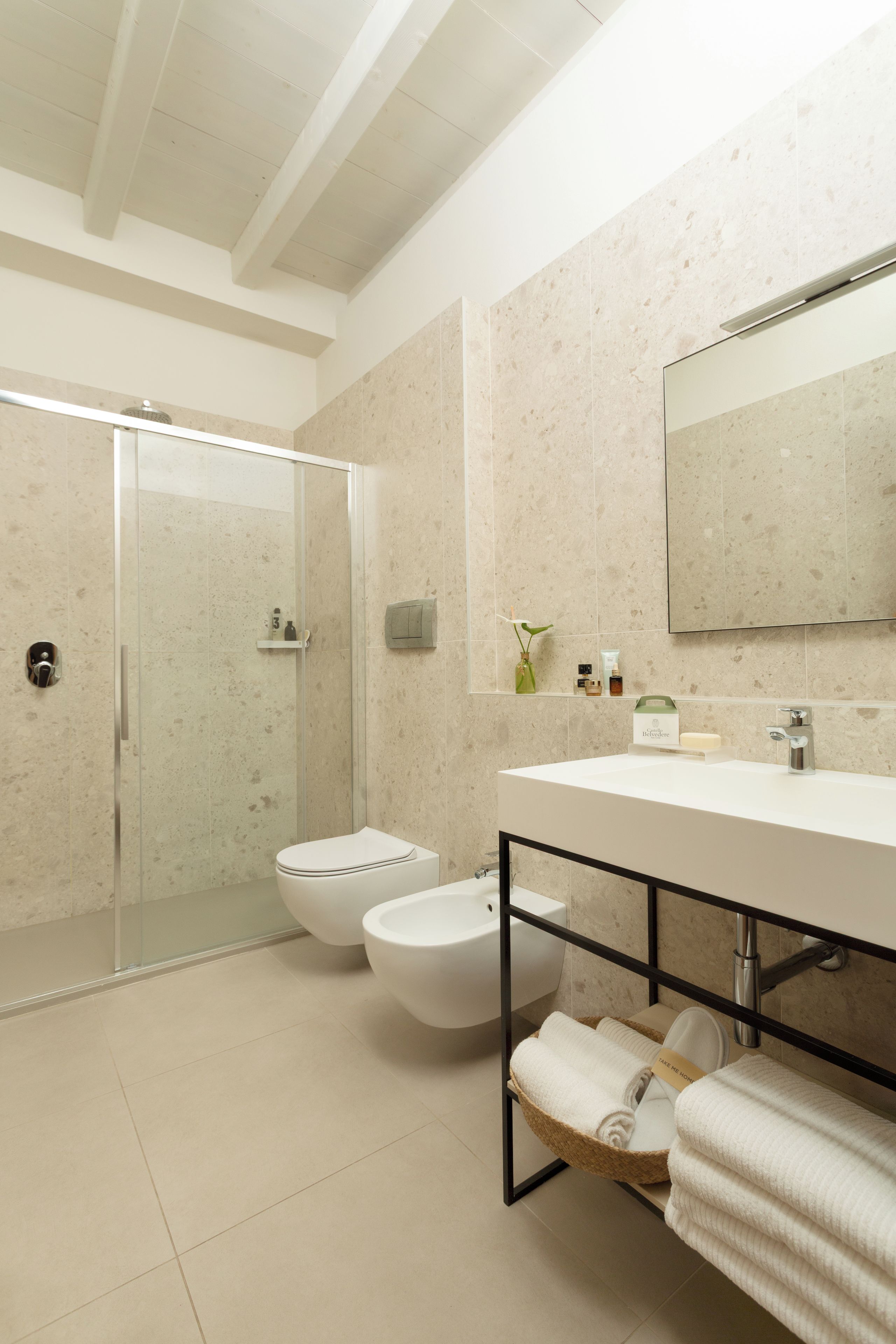 A modern bathroom with a glass shower enclosure, two toilets, a sink with a towel rack, and a large mirror.