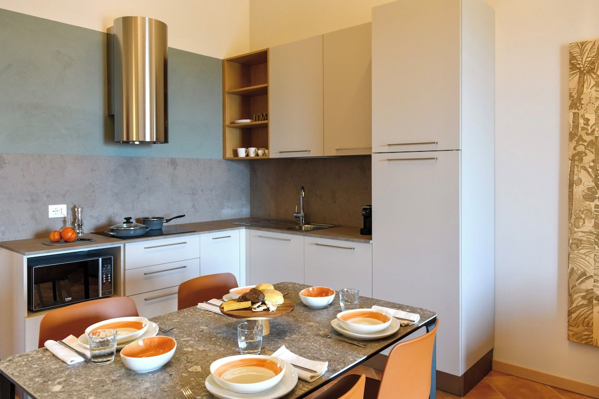 A modern kitchen with a dining table set for four, equipped with a microwave, oven, and a stainless steel range hood.