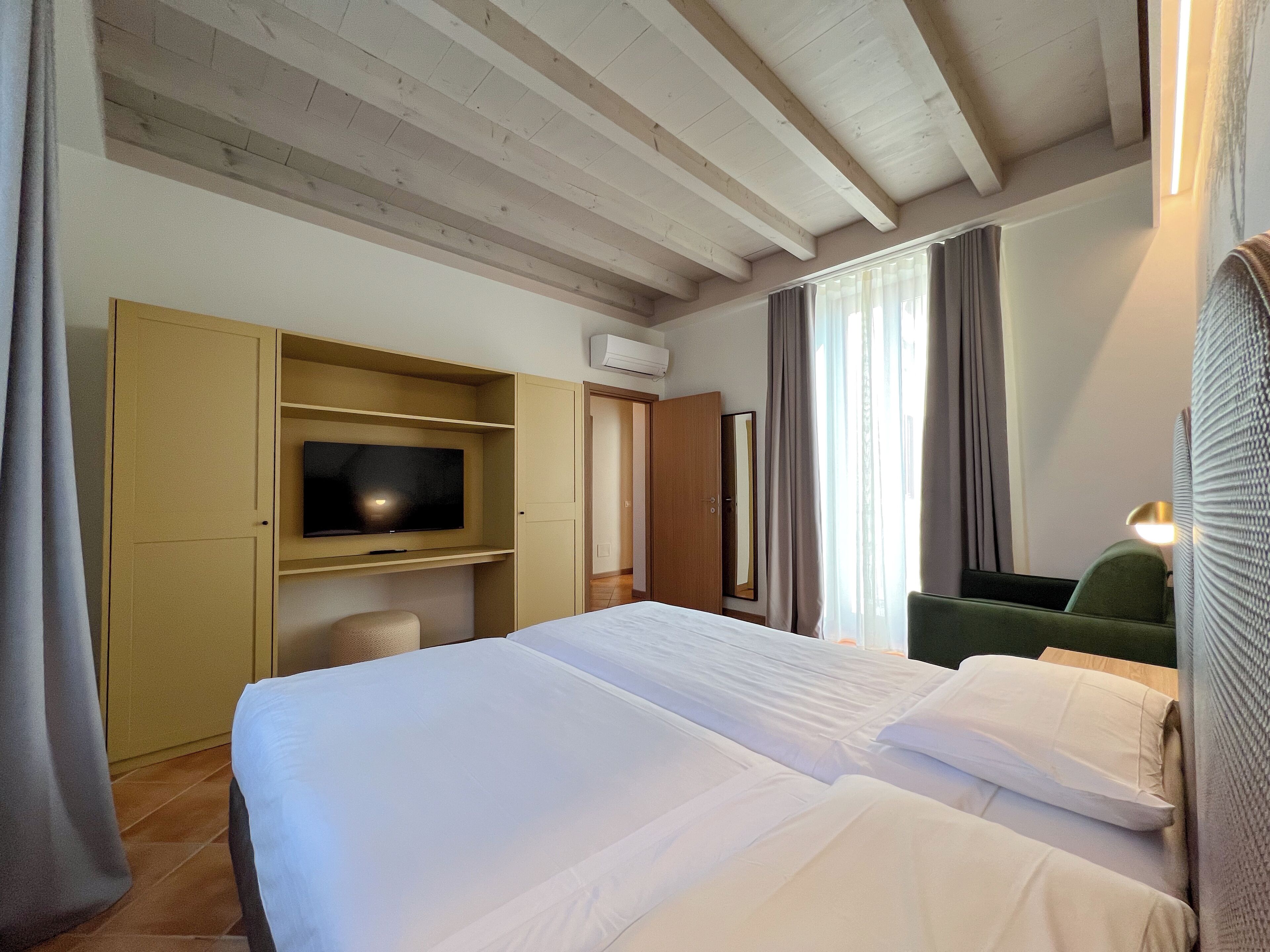 A hotel room with a bed, a television on a shelf, a wardrobe, and a mirror.