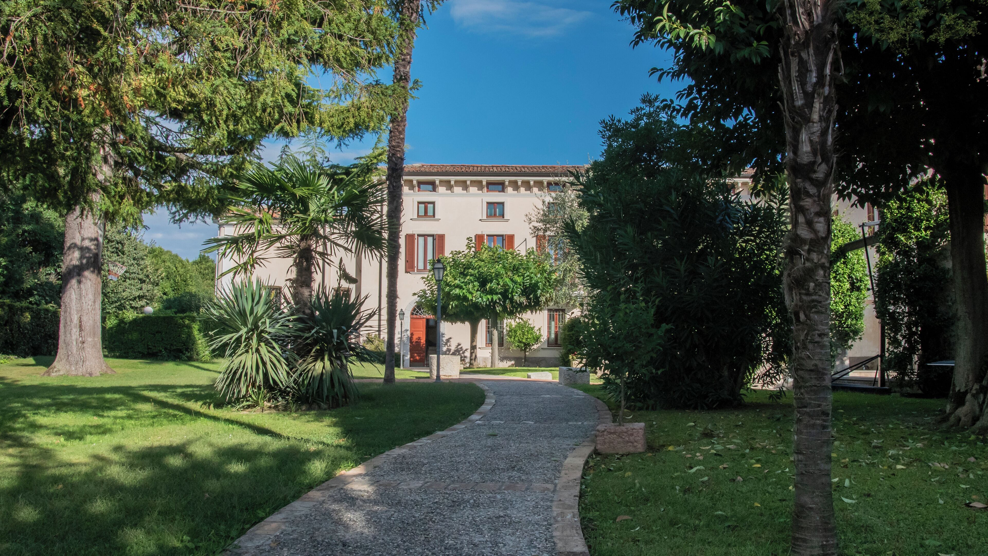 Un chemin menant à un bâtiment à la façade traditionnelle, entouré d’une végétation luxuriante et d’arbres.