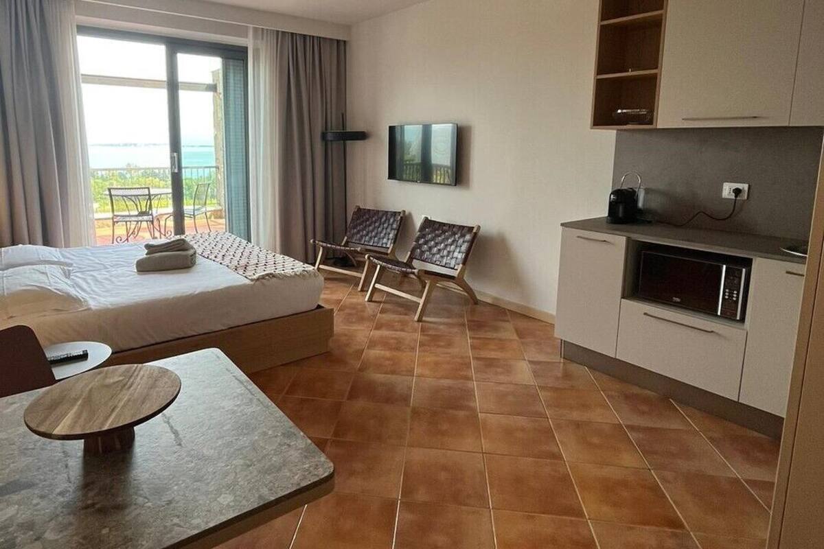 A hotel room with a bed, a dining table, two chairs, a TV, and a kitchenette.