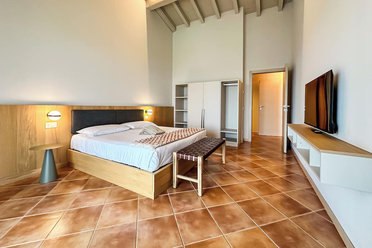 A bedroom with a bed, bedside table, wardrobe, and a TV mounted on the wall.