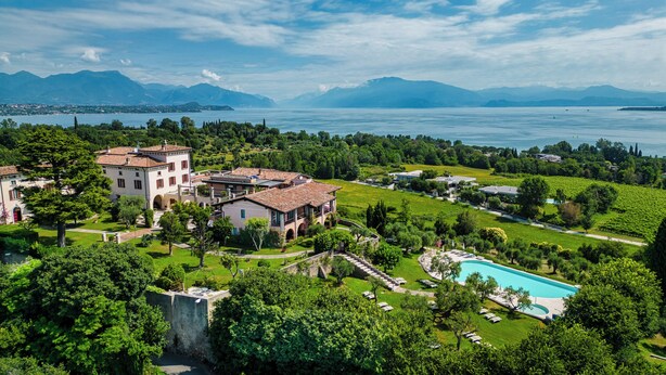 A large estate with a swimming pool, lush gardens, and a view of a lake and mountains.