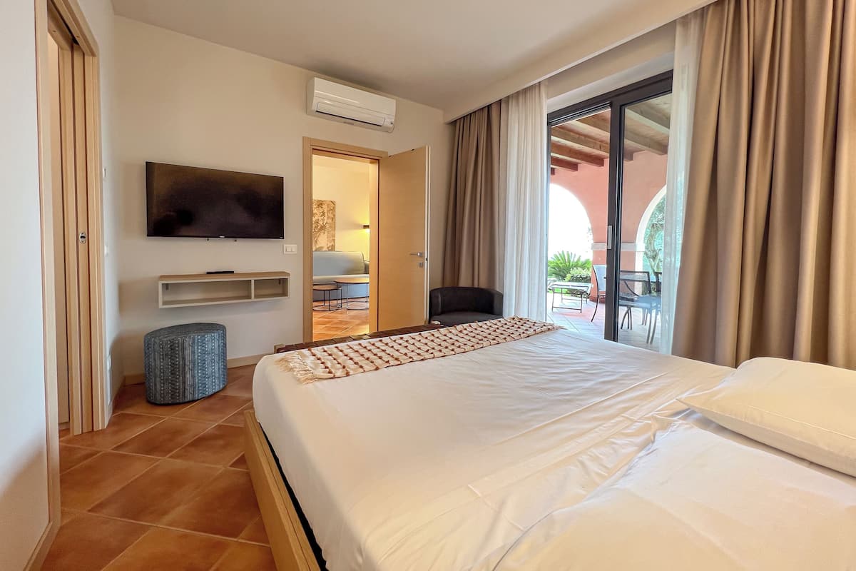 A hotel room with a bed, a TV, a small seating area, and a view of the outside.