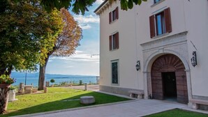 A building with a large arched entrance, a well-maintained lawn, and a view of the sea.