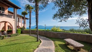 A courtyard with a stone bench, palm trees, and a view of the sea.