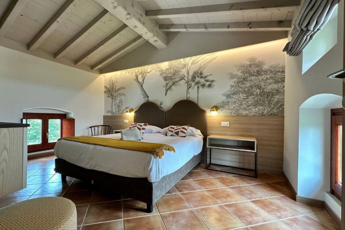 A bedroom with a bed, nightstands, a chair, and a wall with a tree mural.