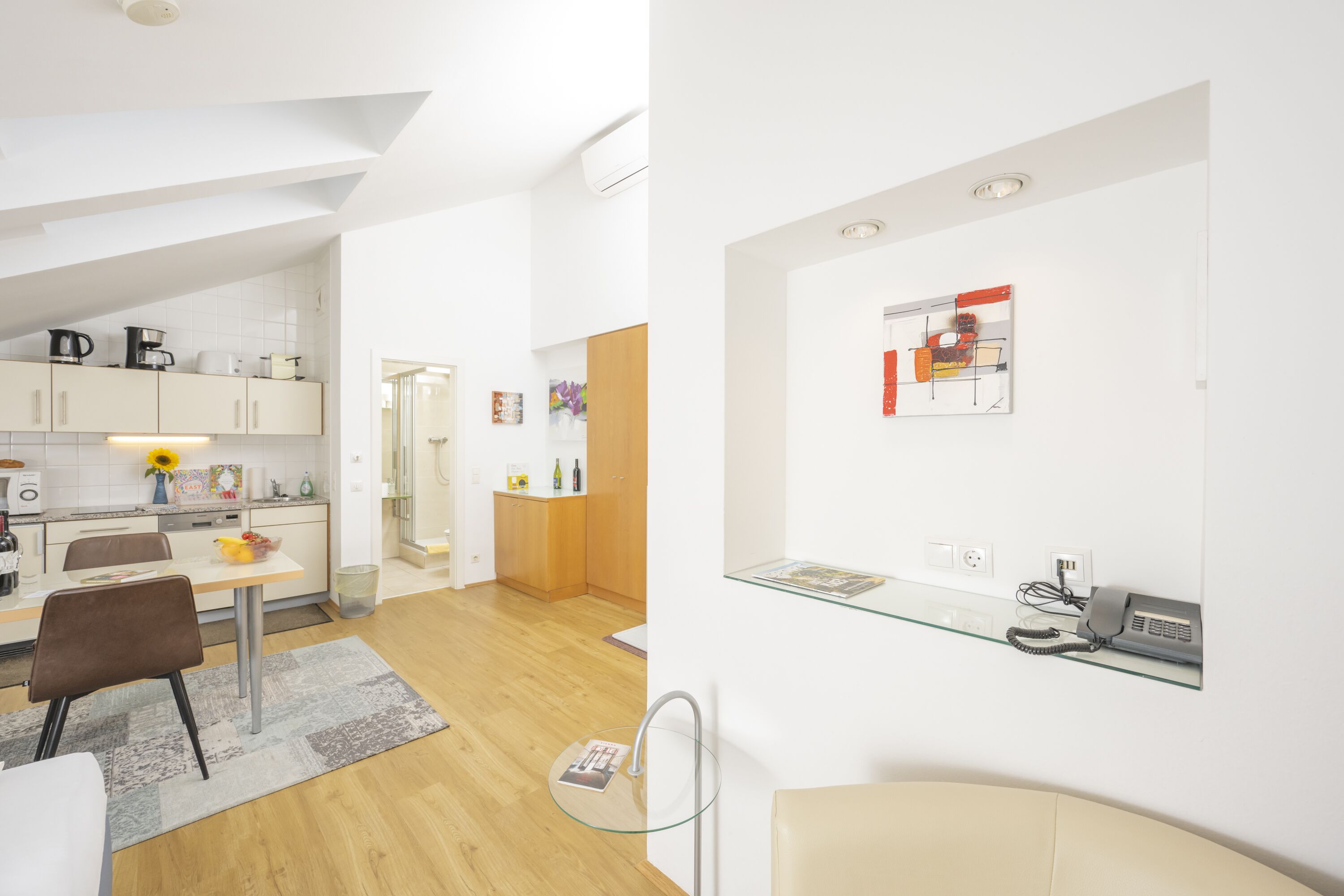 A modern kitchen with white cabinets, a dining area with a glass table, and a living space with a glass coffee table.