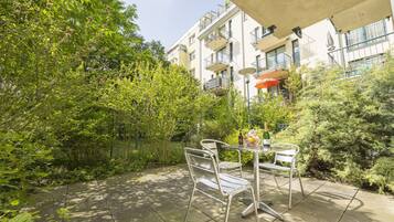 Un patio con sillas y una mesa de metal, rodeado de exuberante vegetación y un edificio con balcones.