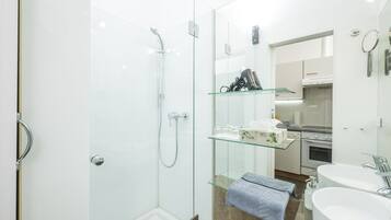 A modern bathroom with a glass shower enclosure, a glass shelf with toiletries, a sink, and a mirror.