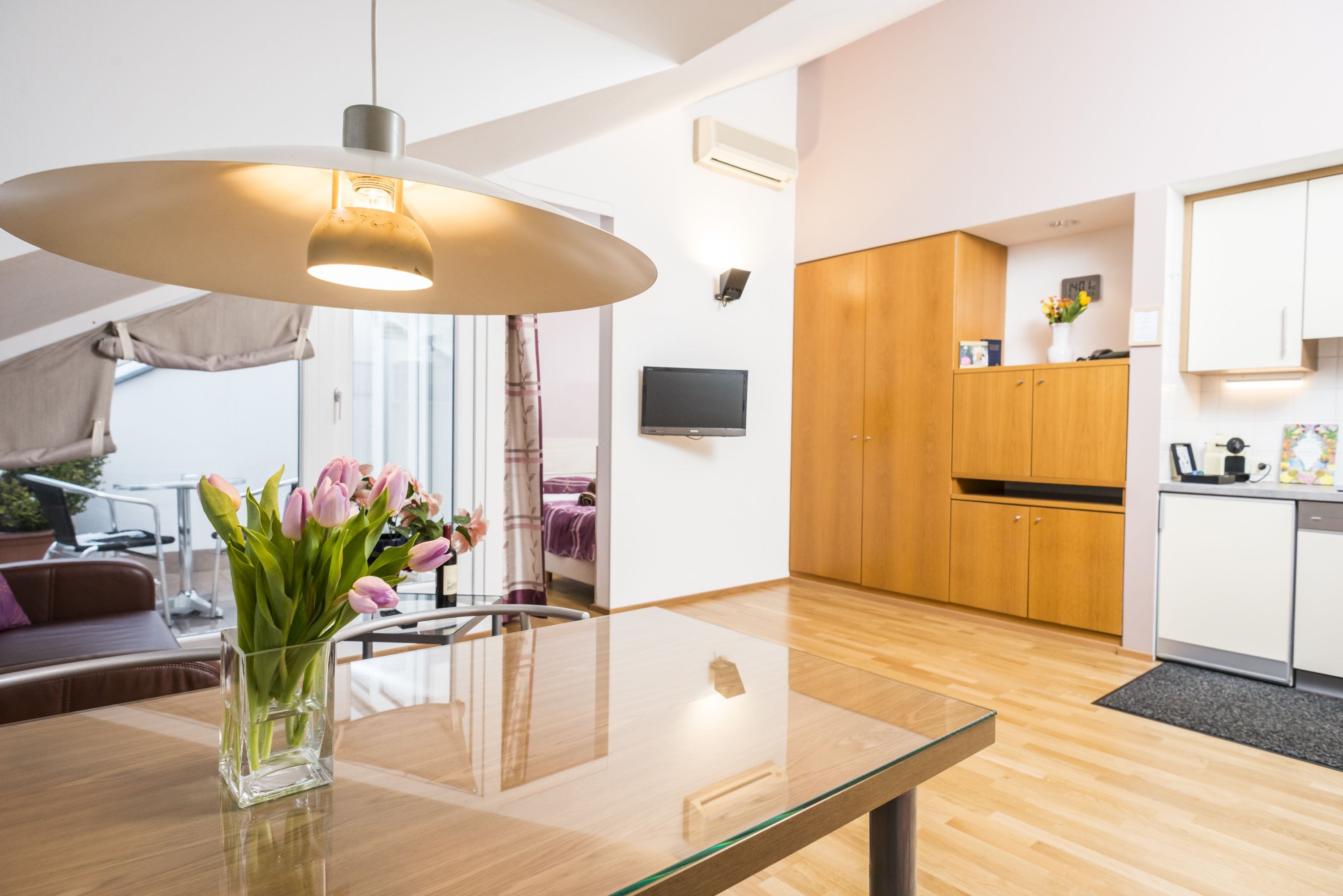A modern kitchen with wooden cabinets, a glass dining table, and a vase of flowers.
