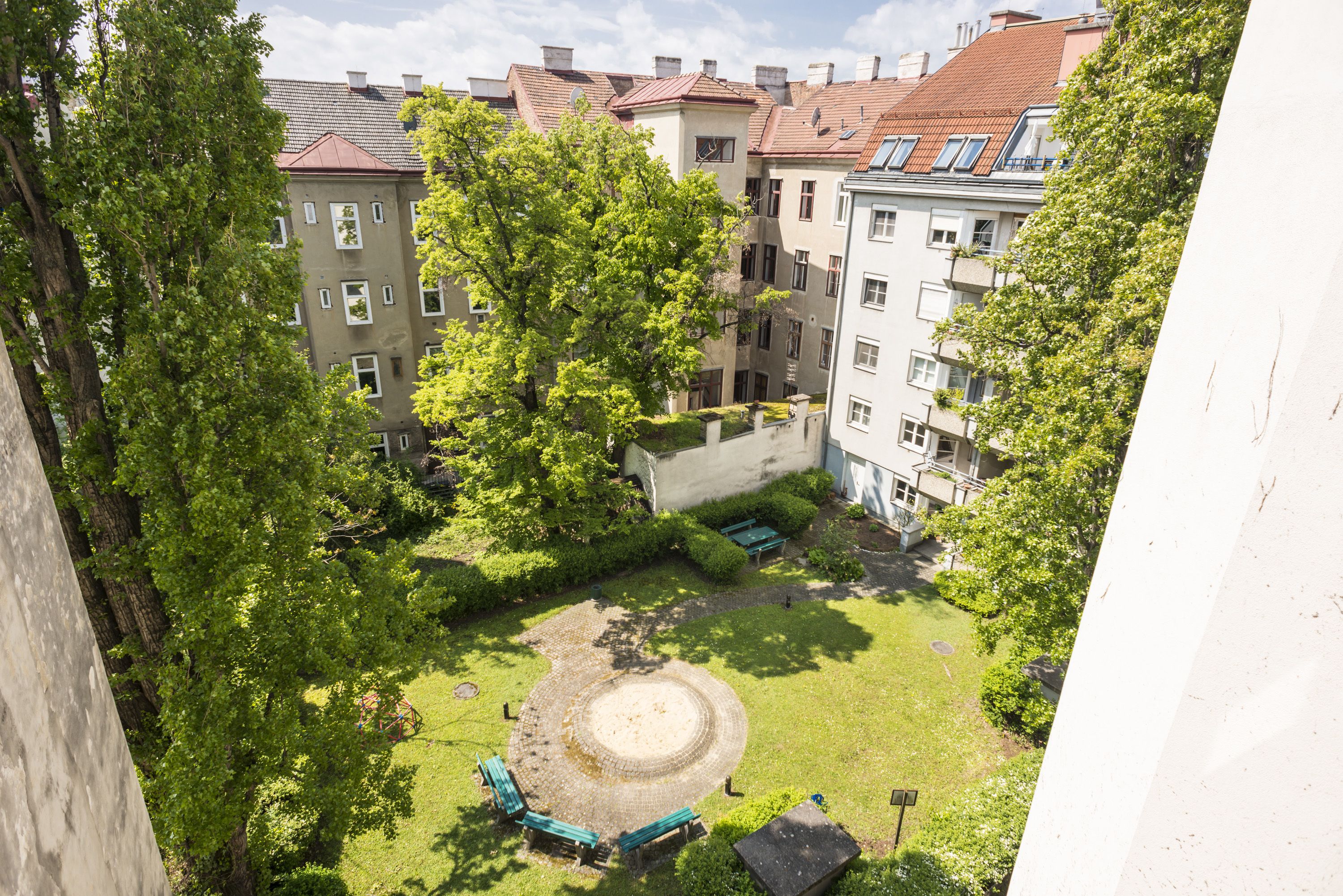 En innergård med en rund sittplats, omgiven av träd och byggnader med röda tegeltak.