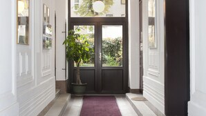 A hallway with a red carpet, a potted plant, and a double door leading to an outdoor area. - Appartements Ferchergasse (Vienna)
