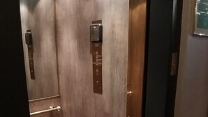 Ein Aufzug mit Holzwänden und einer Metalttür, ausgestattet mit Bedienfeld und Not-Aus-Schalter.