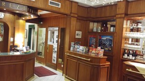 Eine Hotelhalle mit Holzwandverkleidung, einem Empfangstresen, einer Kronleuchter und einer Weinausstellung.